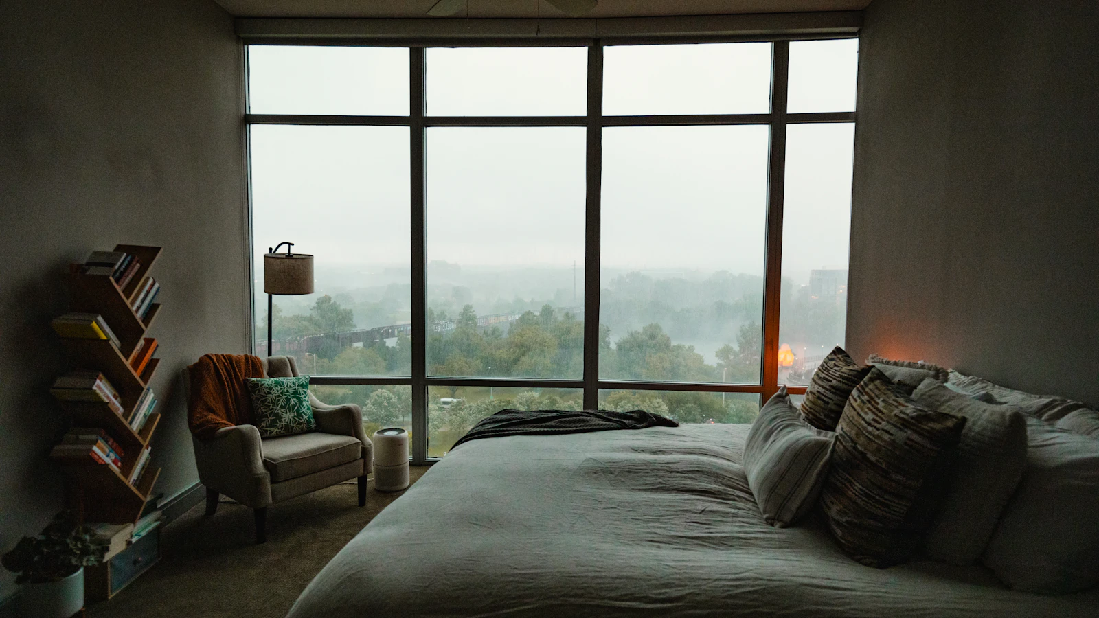 A bed and chair beside large bedroom windows