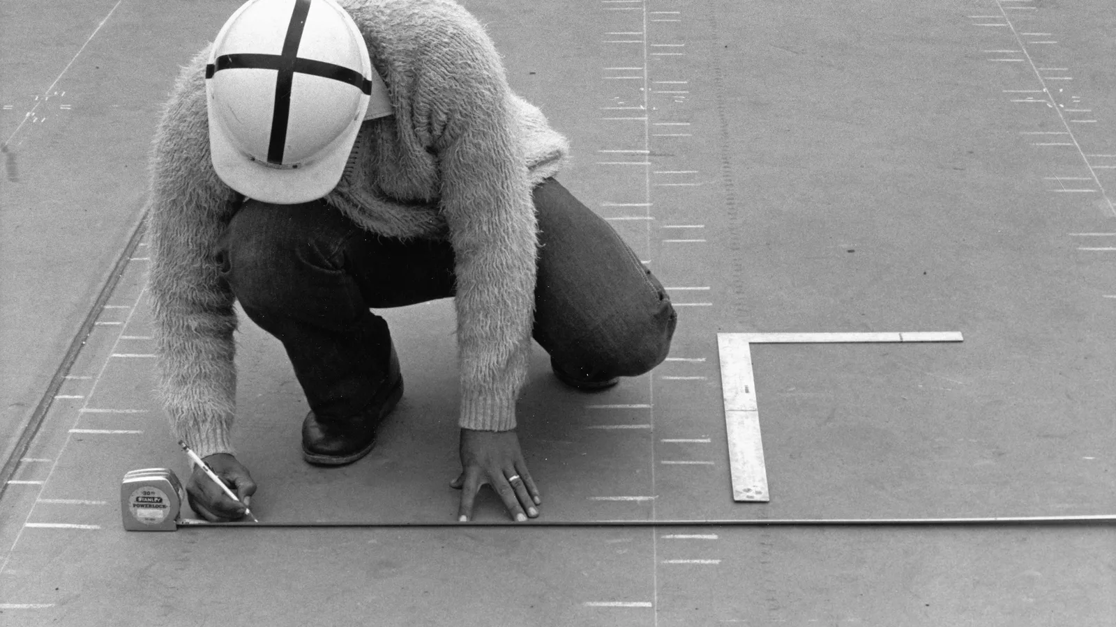 Worker using a tape measure, pencil, and square to mark a large surface