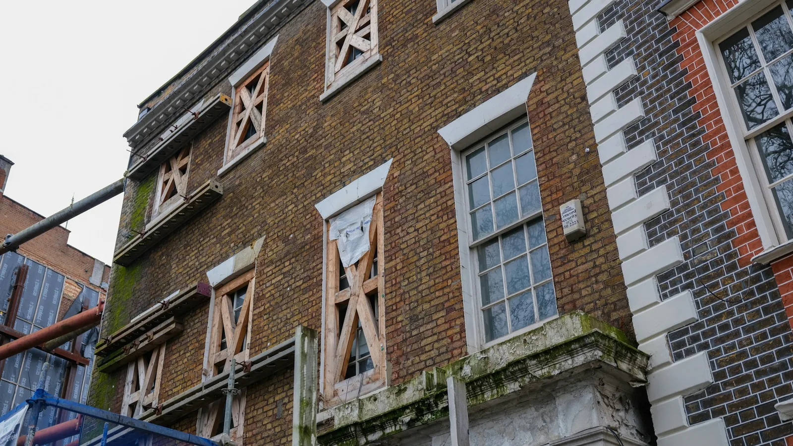 Boarded window openings and scaffolding on a brick building under renovation