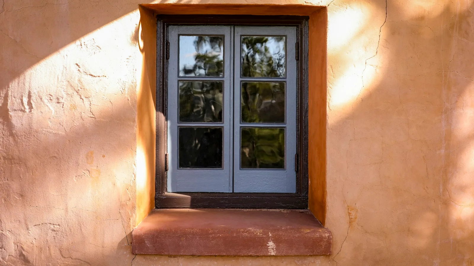 Small divided-light window recessed within a warm-colored stucco wall